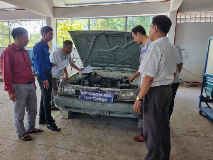 A group of people standing around a car with the hood openDescription automatically generated